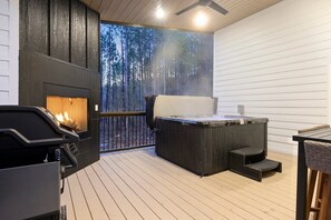 The back covered patio has a hot tub, outdoor fireplace, large smart TV and outdoor dining, with additional seating for enjoying the wooded views!