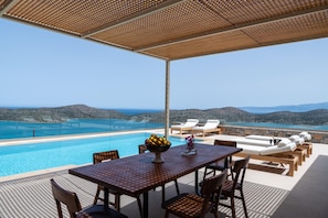 A dining area with seating for six is located under the pergola near the pool.