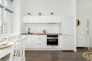 A modern, all-white kitchen with open shelving, built-in appliances, and a sleek design, blending functionality with aesthetic appeal.

