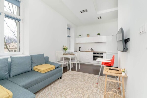 A cozy living space featuring a blue sofa, a white dining table, and minimalist decor, creating a bright and inviting atmosphere.

