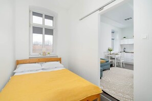 A neatly arranged bedroom with a yellow bedspread, white walls, and a compact yet comfortable layout.

