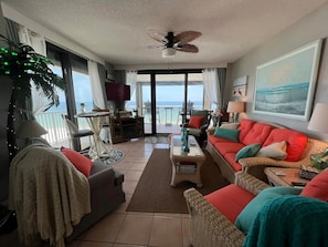 Open living room with lots of comfortable furniture and a wall of windows overlooking the Gulf.