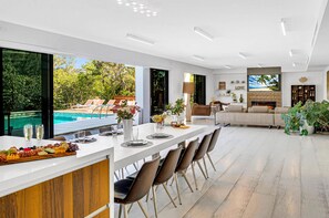 The ample open-concept living, dining, and chef's kitchen area is lined with sliding window walls, offering waterfront views and seamless access to the expansive heated pool.