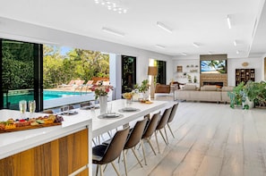 The ample open-concept living, dining, and chef's kitchen area is lined with sliding window walls, offering waterfront views and seamless access to the expansive heated pool.