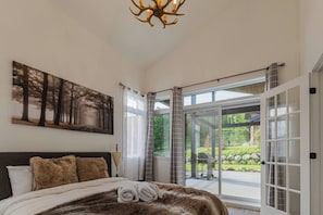 Bedroom with vaulted ceiling, large windows, and direct access to the patio and garden