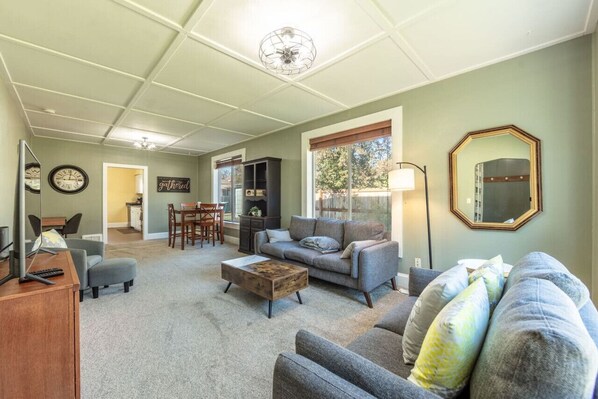 A bright and spacious living room featuring a striking accent ceiling that adds character and style. The sleek, updated furniture creates a modern and comfortable atmosphere. The open layout provides plenty of room to spread out and enjoy the space.