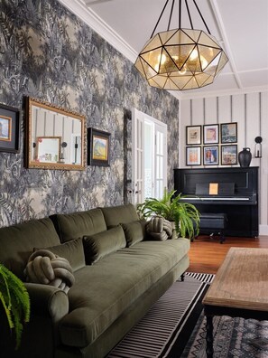 That green velvet sofa and jungle wallpaper combo is stunning. The pendant light and piano add a classy, tropical vibe. Total vintage charm.