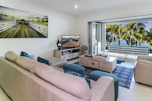 The living area offers a lounge and arm chair fronting a central TV. Bi-fold doors open up to let in the refreshing sea breeze.