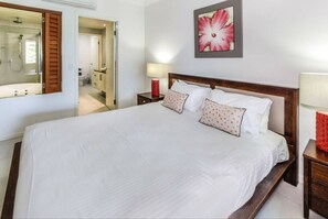 The primary bedroom offers a king-sized bed and connects to an open-air ensuite with a glass shower and jetted spa bath.