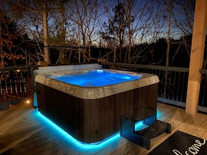 Serene hot tub on deck, glowing blue, surrounded by peaceful forest at night.