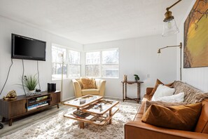 This cozy living room features two large windows filling the space with natural light. A plush leather couch sits atop a soft carpet, complementing a beautiful coffee table. A sleek TV completes the setup, offering relaxation and entertainment.