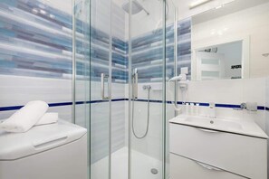 A contemporary bathroom with a spacious shower cabin, blue and white tiles, and essential toiletries provided for guests’ convenience.