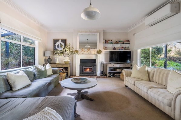 In the main house, a second living area features a cosy fireplace, air conditioning, two sofas, a chaise lounge, and a TV.