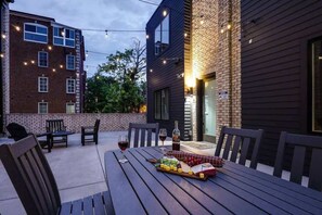 SHARED outdoor patio space draped in bistro lights with outdoor dining table, lounge area, fire pit, and BBQ Grill