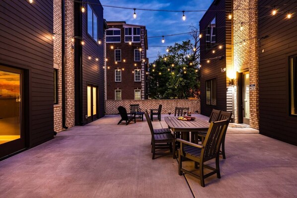 SHARED outdoor patio space draped in bistro lights with outdoor dining table, lounge area, fire pit, and BBQ Grill