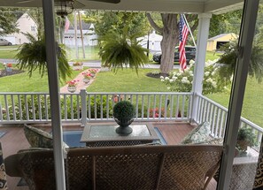 Relax on the serene porch with a view of a beautifully manicured lawn and vibrant flower beds, an idyllic spot for morning coffee or evening reflections on Conesus Lake. 