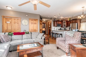 Open concept living room, kitchen. Bar seating with stools in kitchen area. L shaped sofa and oversized chair in living room.