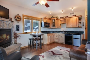 Living/dining area opens up to efficiency kitchen. Stone gas fireplace, bar table with seating for four.