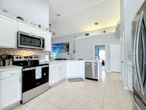 - Sleek white cabinetry and stainless steel appliances create a clean, coastal look
- Fully stocked with cookware and utensils for whipping up family meals with ease
- Tropical wall art and light tile flooring complete the bright, breezy vibe