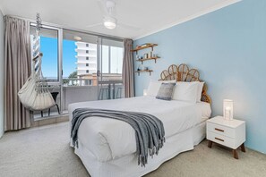 The first bedroom features a queen-size bed and a cosy swing chair with ocean views. 
