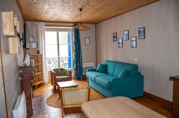 Salon détente avec canapé convertible, deux fauteuils, TV 4k et un balcon.