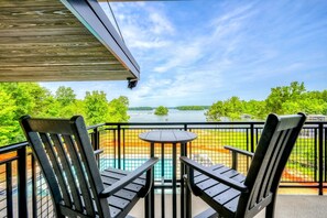 A tranquil lakeview from a high balcony seating area, with a wooden overhang and black metal railing, inviting relaxation and contemplation of the natural surroundings.