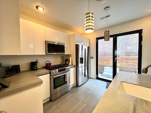 Modern gloss kitchen with marble countertops with island. Gas stove, microwave, oven, refrigerator, toaster and coffee maker. Dinnerware and silverware for up to 8 guests. Folding kitchen door opens to private step-down patio backyard with gas grill.