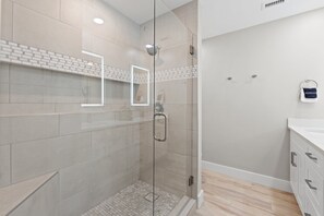 Oversize tiled step in shower has a rain shower head and shower seat and shower ledge for bath accessories.