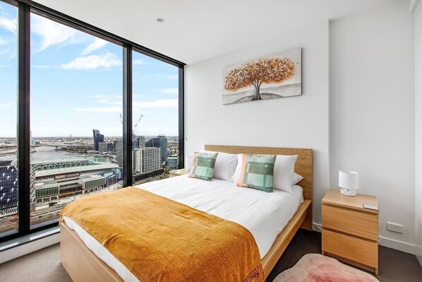 The light and airy bedroom features a queen-size bed with sweeping views overlooking Marvel Stadium and the Yarra River. 
