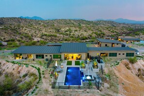 Stunning private oasis featuring a sparkling heated infinity pool and spa with sun loungers, a patio with a BBQ grill, multiple lounge areas, and fire pits surrounded by unparalleled desert views.