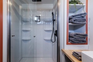 The bathroom features a spacious shower with hot and cold water, fresh towels, and complimentary shampoo. A stylish mirror provides convenience, while ample storage keeps essentials organized. 