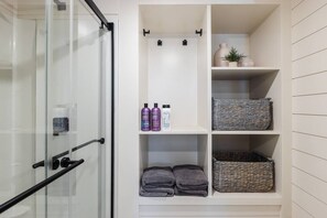 The bathroom features a spacious shower with hot and cold water, fresh towels, and complimentary shampoo. A stylish vanity and mirror provide convenience, while ample storage keeps essentials organized. 