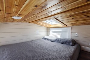 Enjoy a restful night on a comfy queen-sized bed with soft, crisp linens. A plush mattress ensures support and comfort, while a skylight window above lets you drift off under the stars and wake up refreshed, ready to take on the day.