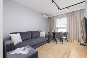 A spacious and modern living room with a gray sofa, a TV, and a large window allowing plenty of natural light.