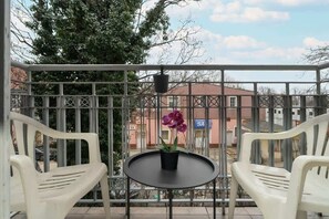 A charming balcony with a wrought iron railing, a small table, and chairs, offering a pleasant outdoor retreat with city views.

