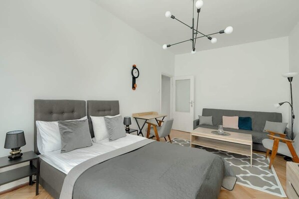 A bright bedroom with a comfortable double bed, modern lighting, and a cozy seating area, combining elegance with relaxation.

