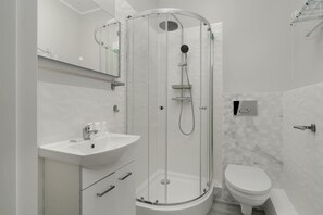 A sleek bathroom featuring a glass shower cabin, white tiles, and modern fixtures, providing a fresh and clean atmosphere.

