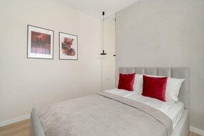 A bedroom with a large bed covered with white bedding and red pillows, complemented by wooden cabinets above the bed.