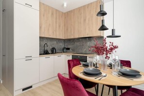  A kitchen and dining area with a light wood dining table, red chairs, and stylish pendant lights. There's a vase with red flowers on the table.
