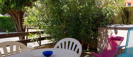 Terrasse avec store banne, barbecue charbon, table à manger et chaises longues.