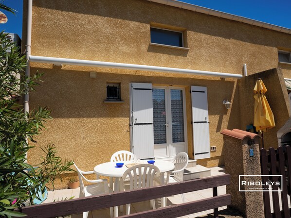 Terrace with awning, charcoal barbecue, dining table and sun loungers.