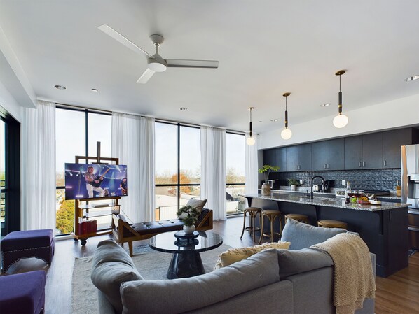 Open floor plan living area with floor-to-ceiling windows, comfortable seating, smart TV, and access to the private balcony.