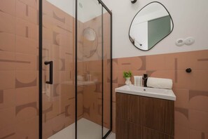A modern bathroom with terracotta tiles, a glass-enclosed shower, a round mirror, and a sleek vanity.

