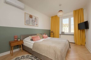 Another bedroom angle, featuring a green accent wall, a wooden nightstand, and a cozy bed with soft, neutral bedding.

