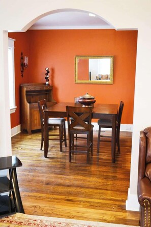 Step into a cozy living space—couch, table, chairs—a gateway to a charming dining room through an elegant archway. Reflect in the dining room's ambiance, adorned with a mirror. A perfect home-stay ensemble for comfort and style.