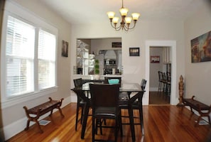 A charming dining haven—hardwood floors, white walls, a centerpiece table, and chairs. Above, a dazzling chandelier illuminates elegance. This room beckons in its simplicity, turning every meal into a delightful experience.