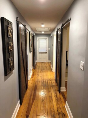 Enter an elegant journey through a long hallway, its wooden floor gleaming with warmth. Sliding doors unveil hallways leading to a door adorned with a window, promising a graceful transition between spaces and an abundance of natural light, crafting an in