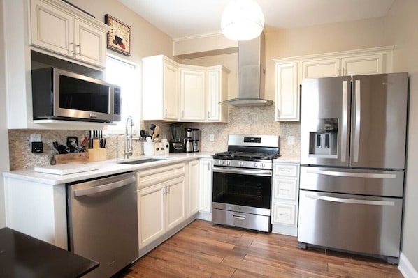 The kitchen is modern and inviting, with cream cabinets and stainless steel appliances, including a dishwasher, microwave, gas stove, and French door refrigerator. A mosaic tile backsplash and hanging pendant light add stylish accents to the space.