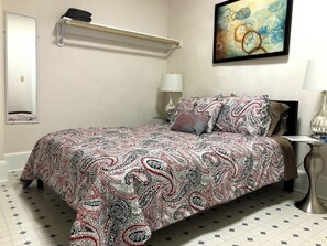 The bedroom features a neatly made bed with a paisley-patterned bedspread, flanked by two matching nightstands with elegant silver lamps. An abstract painting hangs above the bed, enhancing the room's refined aesthetic.