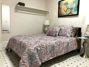 The bedroom features a neatly made bed with a paisley-patterned bedspread, flanked by two matching nightstands with elegant silver lamps. An abstract painting hangs above the bed, enhancing the room's refined aesthetic.